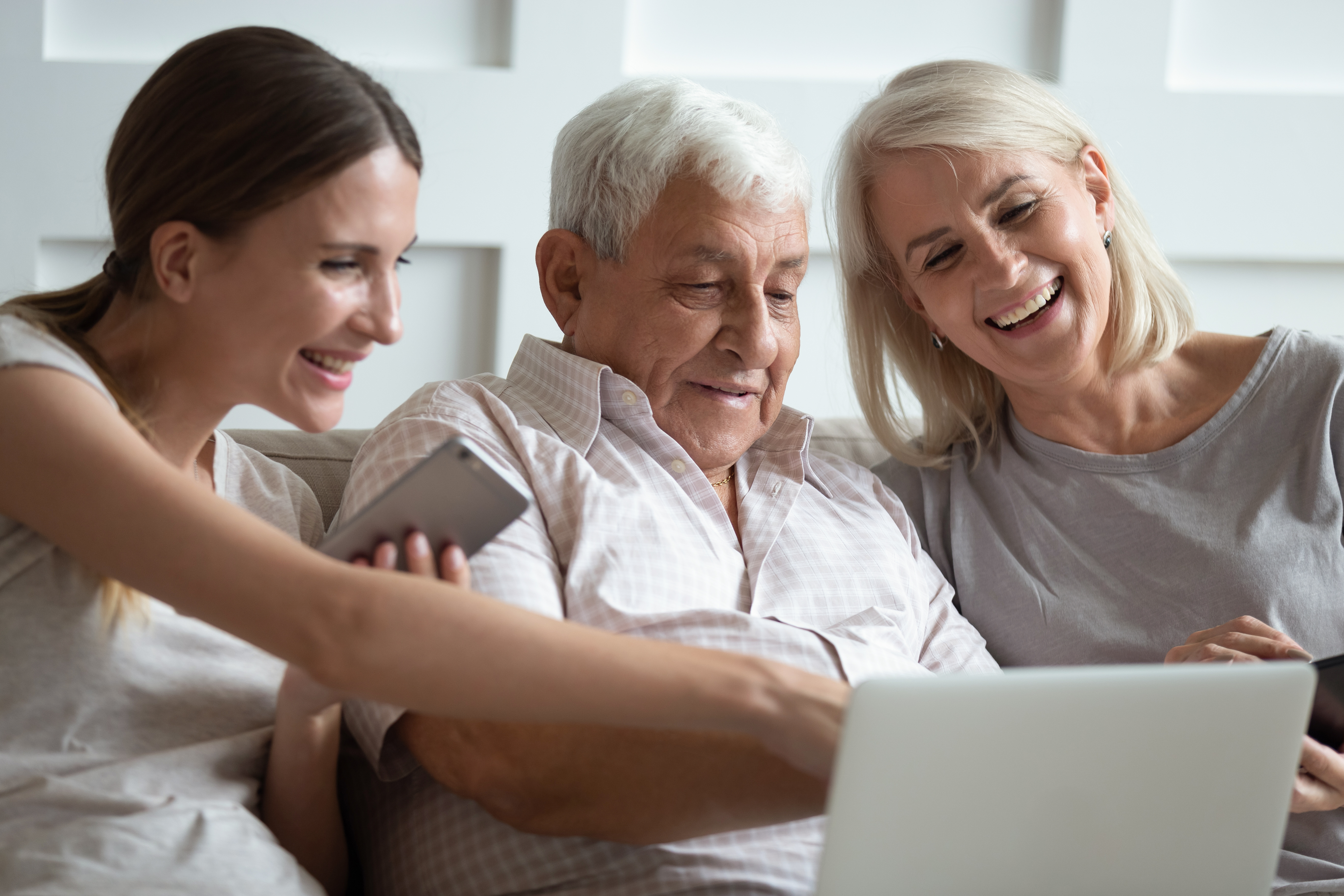 Two middle-age woman showing an elderly man a laptop