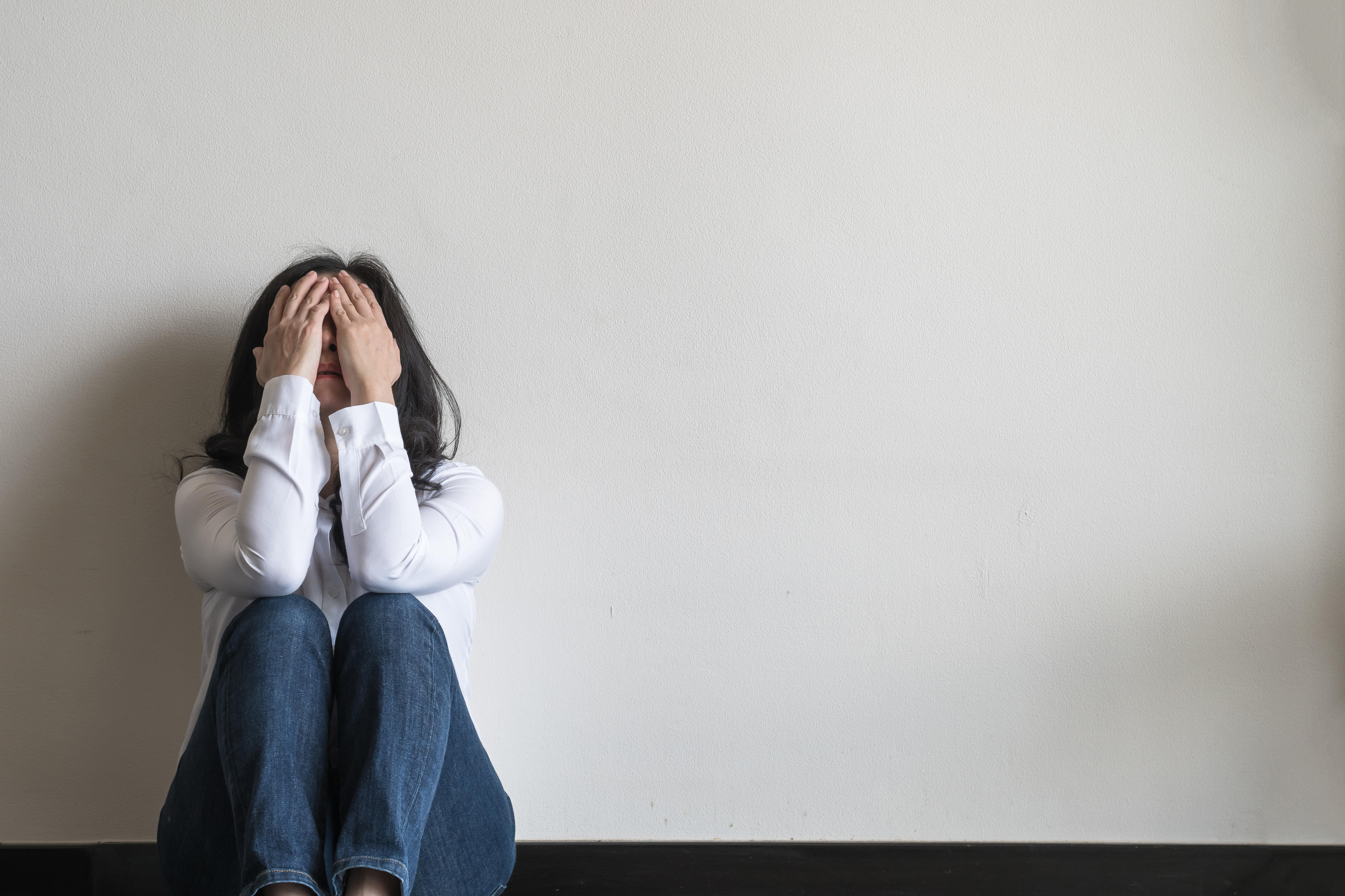 woman sitting against a wal and covering her face